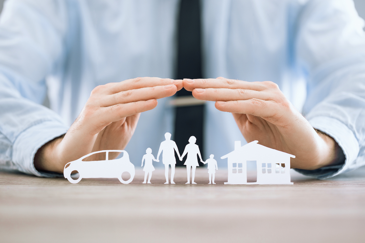 Pessoa com as mãos protegendo ícones de carro, casa e família, representando segurança e proteção por meio de seguros.