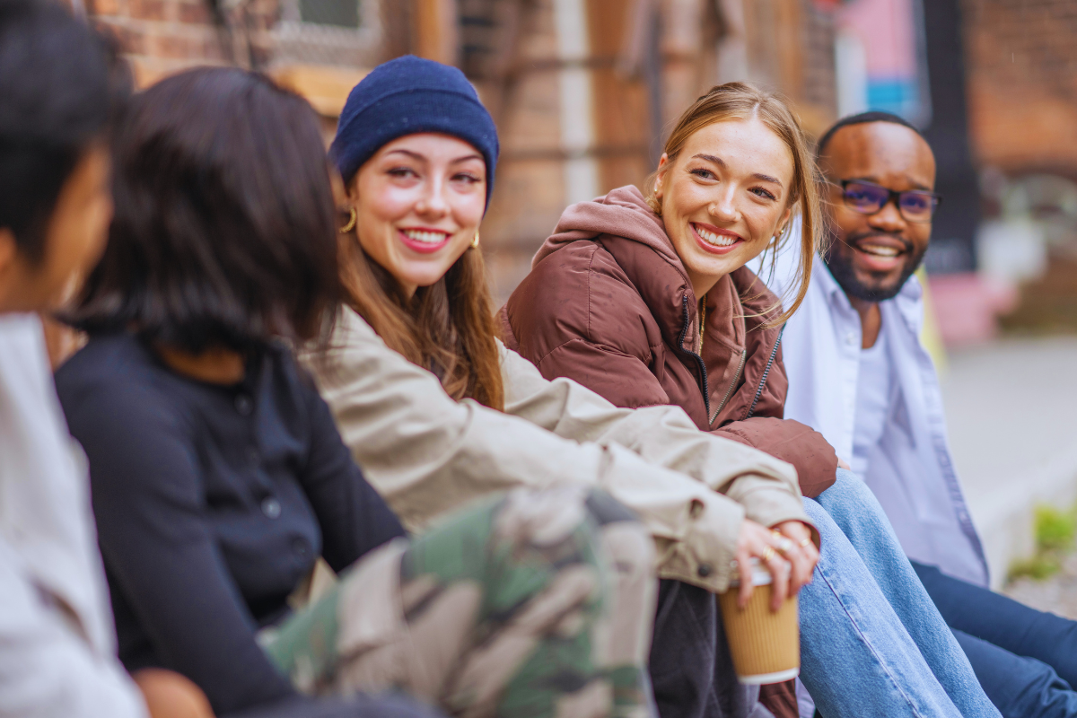 Grupo de jovens sorrindo enquanto conversam ao ar livre.